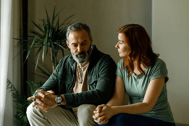 A couple sitting together in conversation beside a houseplant