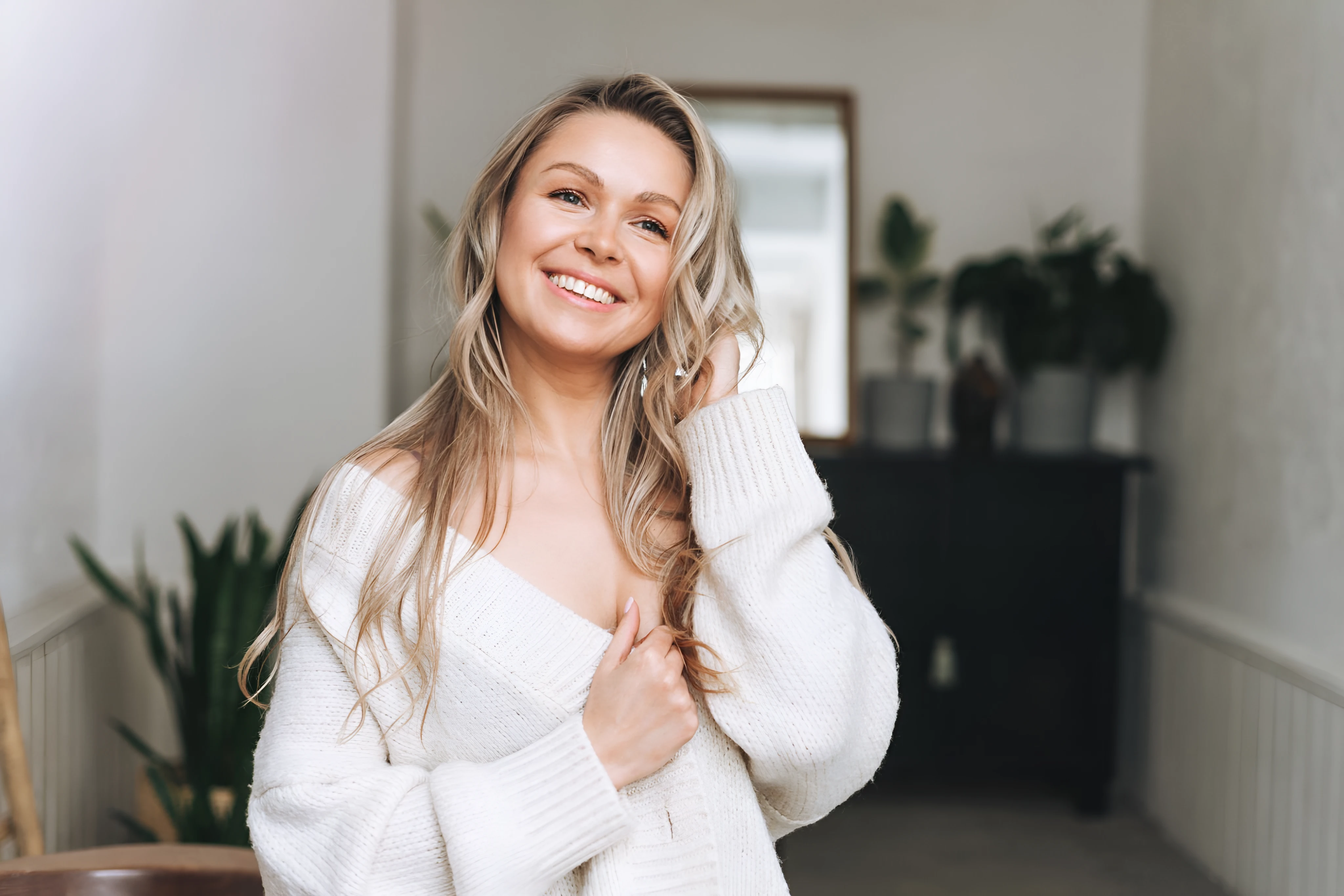Mujer sonriente con un suéter blanco en un pasillo luminoso