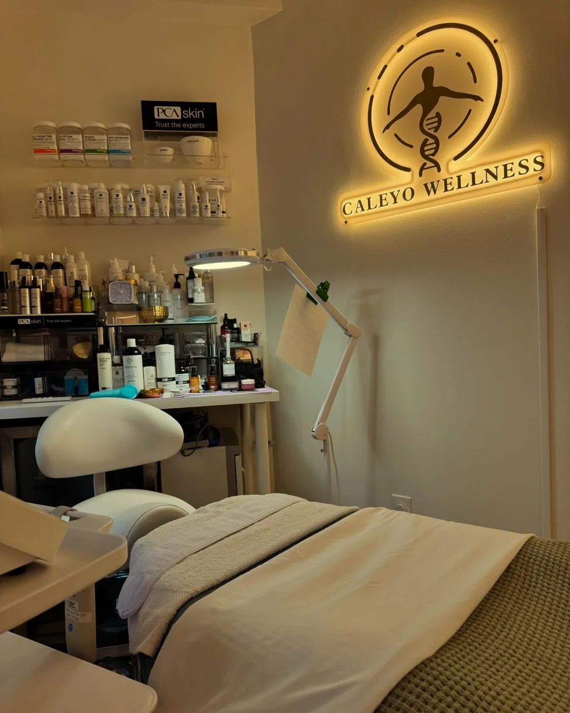 Sala de tratamiento de Caleyo Wellness con una camilla bajo el letrero iluminado de Caleyo