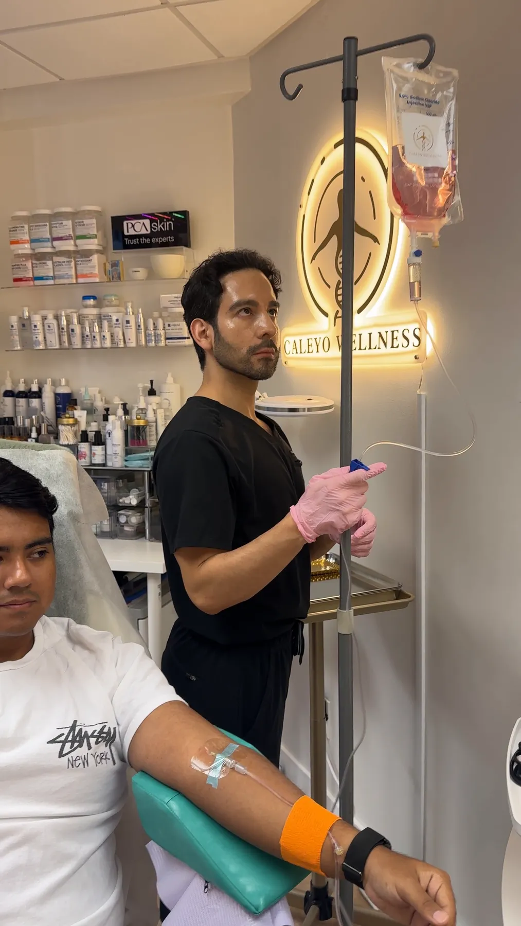 Un clínico con uniforme negro ajusta una infusión IV para un paciente en Caleyo Wellness